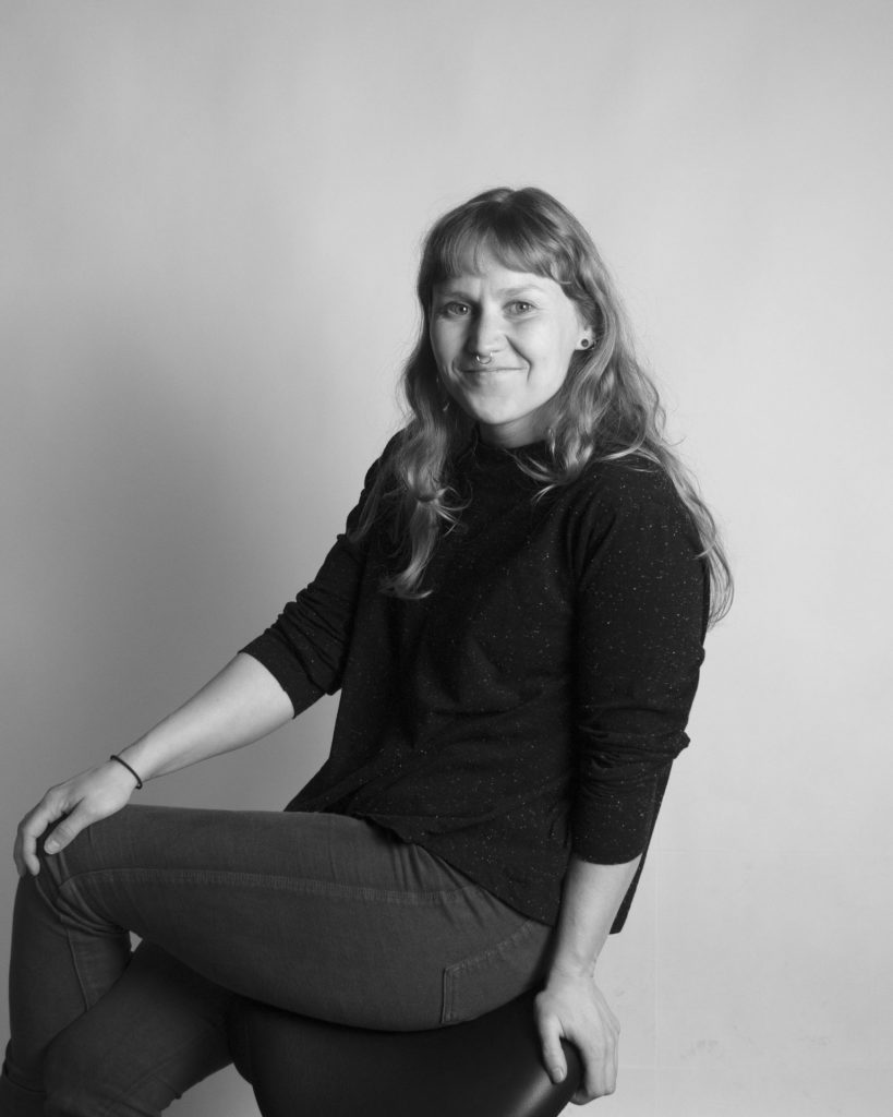 Portrait picture of a woman sitting on a chair smiling towards the camera.