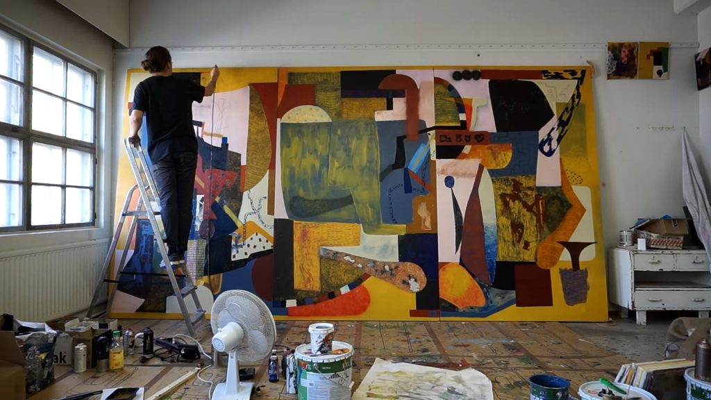 Artist J.P Köykkä standing on a ladder painting a big and colorful abstract artwork in his studio space.