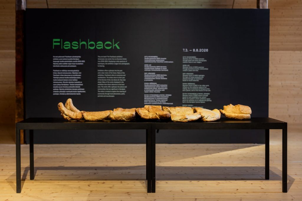 Exhibition space that has a sculpture on the front of the image. A person made of bread is on the table 