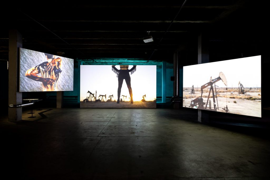 kolme videoteusta tilassa jossa ihmisiä