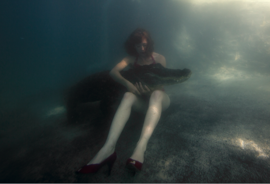 nainen istuu vedenalla pidellen sylissään krokotiiliä