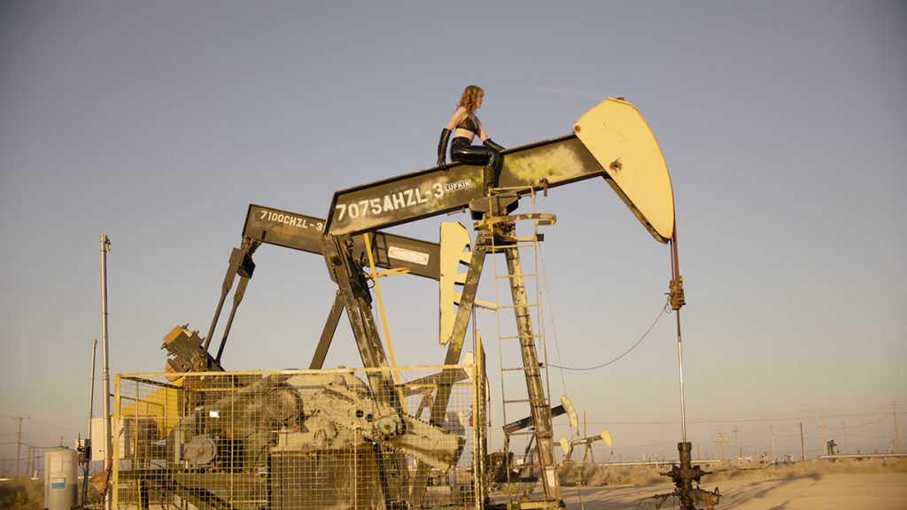woman sitting on top of the oil drilling machine in the desert.