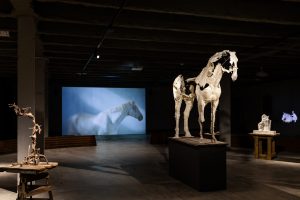 Horse sculpture and behind it a video of a horse in a exhibition space