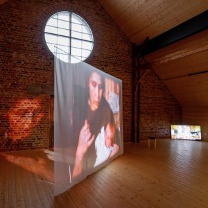 Exhibition space with a big round window. Video screening in the space that has a screenshot of woman with a baby. 