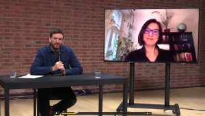 man speaking behind the desk, woman picture on a screen