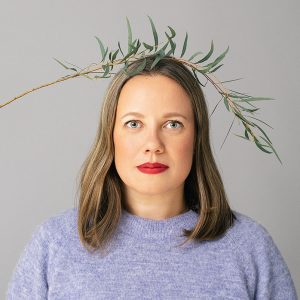 nainen katsoo suoraan eteenpäin. Pään päällä oksa taipuneen. 