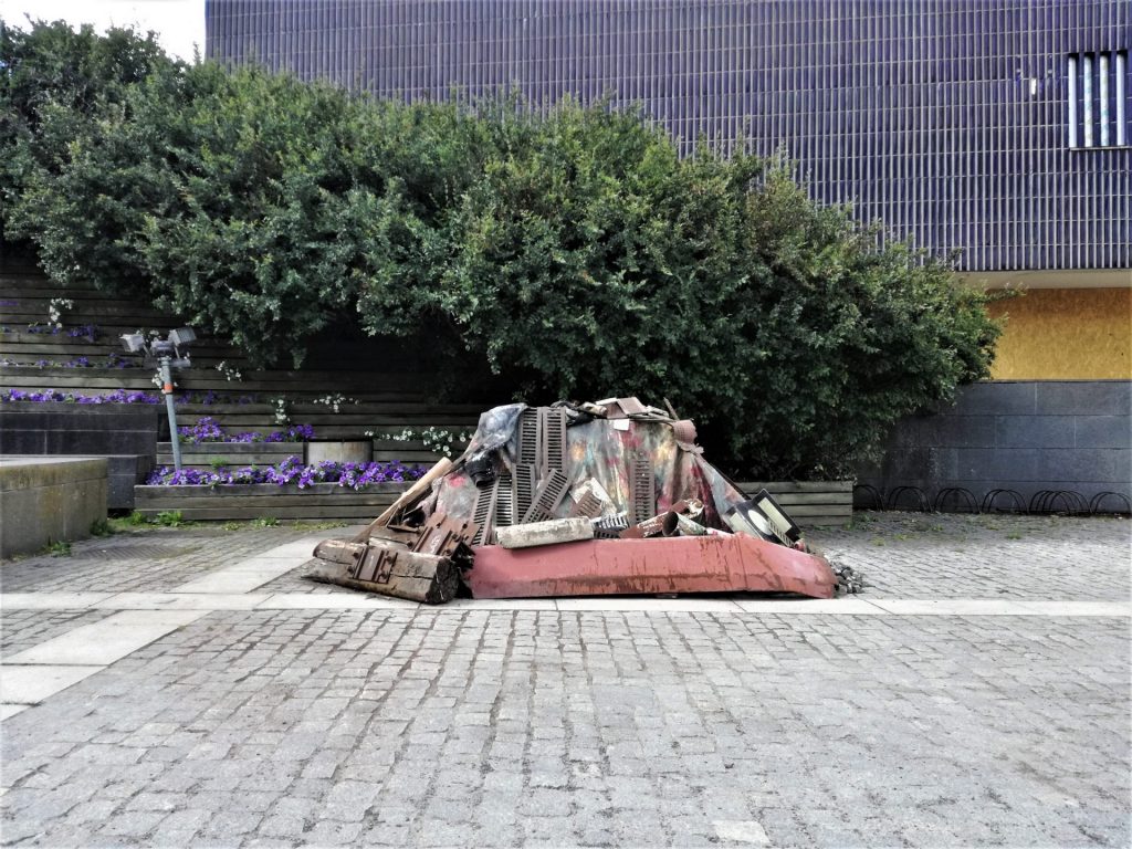 A sculpture made out of recycled material in front of a building