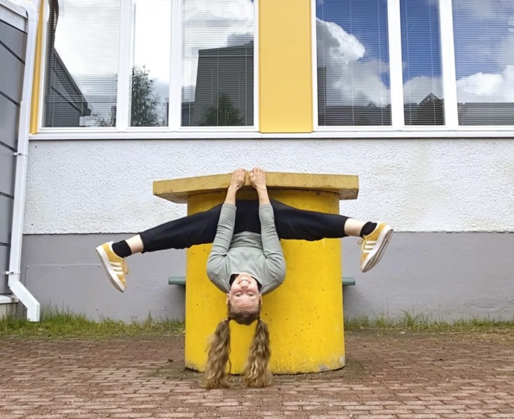 Woman hanging upside down while doing a split on a concrete block next to a building